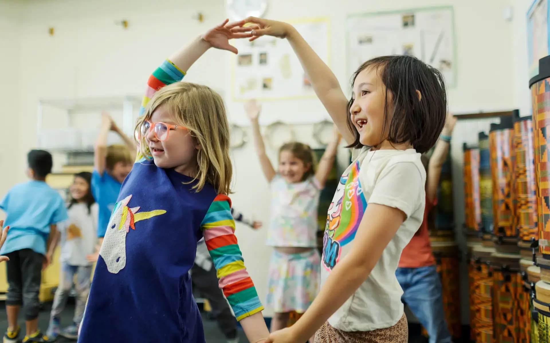 Two Lower School girls join hands over their heads, smiling, in Music class. 