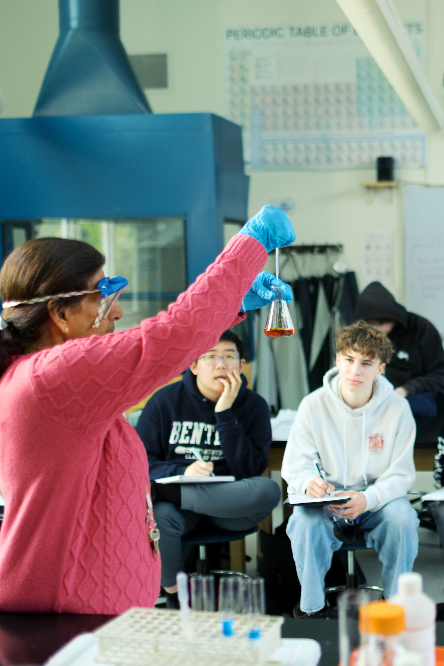 teacher holding up a beaker of liquid while high school students take notes during a chemistry demonstration
