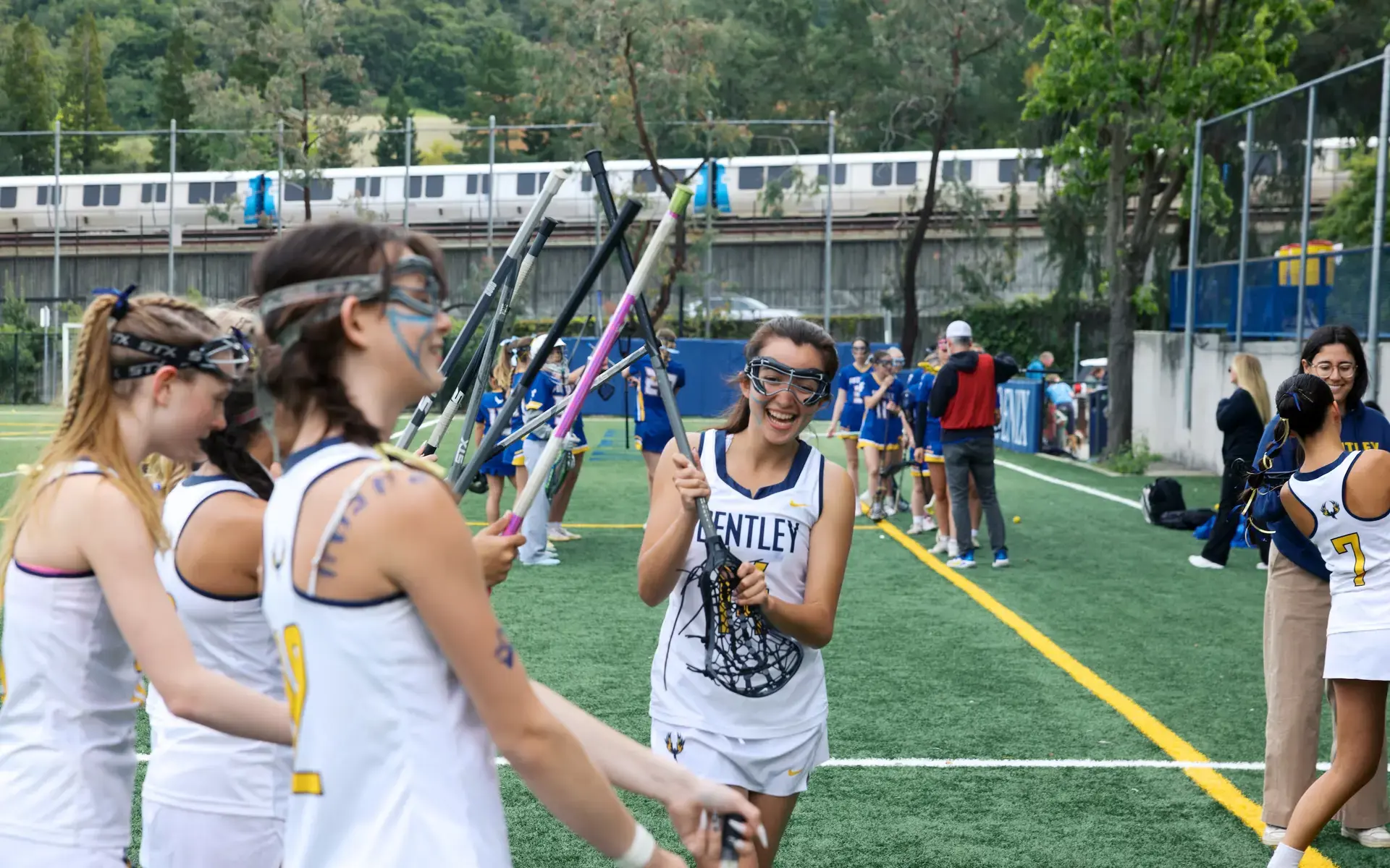 Girls' Upper School Lacrosse player runs by cheering teammates holding up her lacrosse stick. 