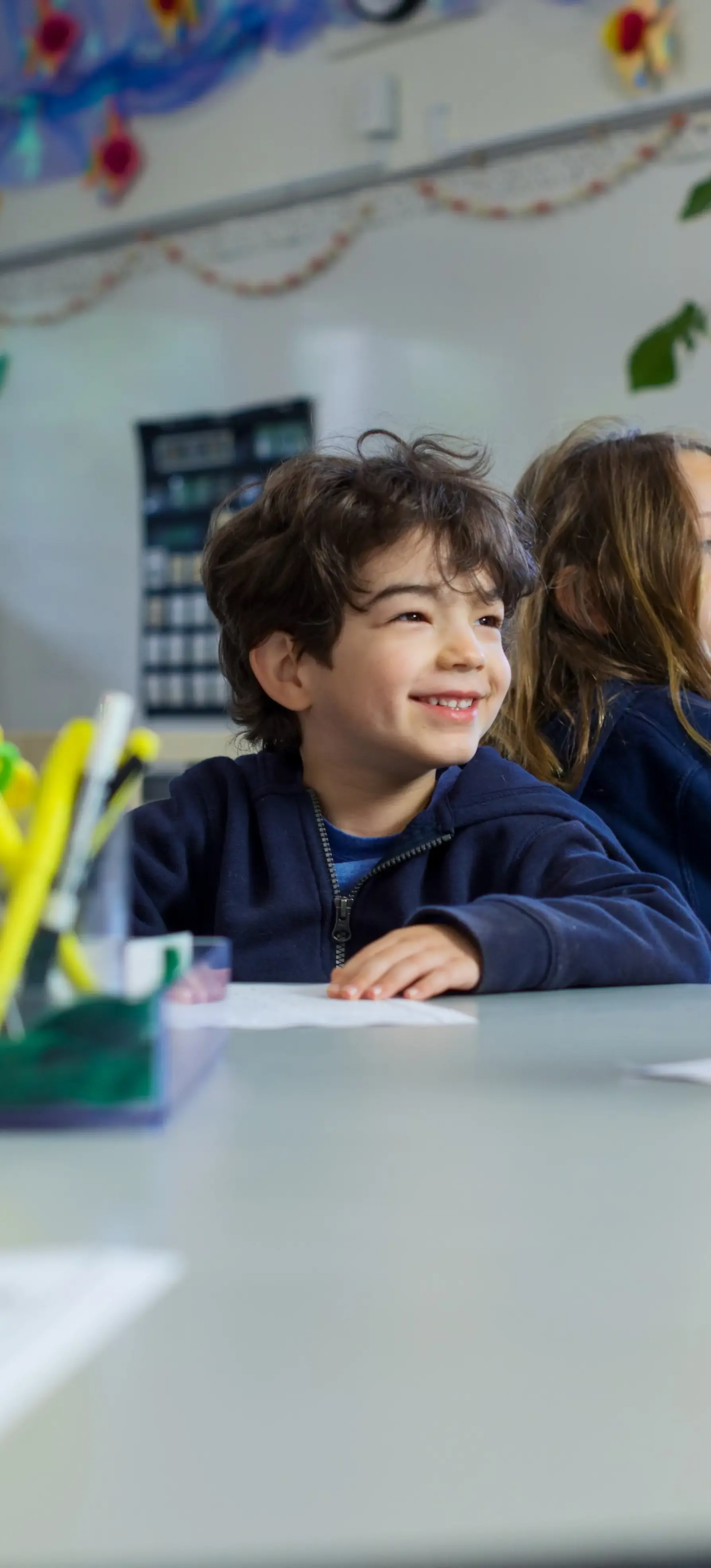 Kindergartner sitting at a table looking ahead and smiling. 