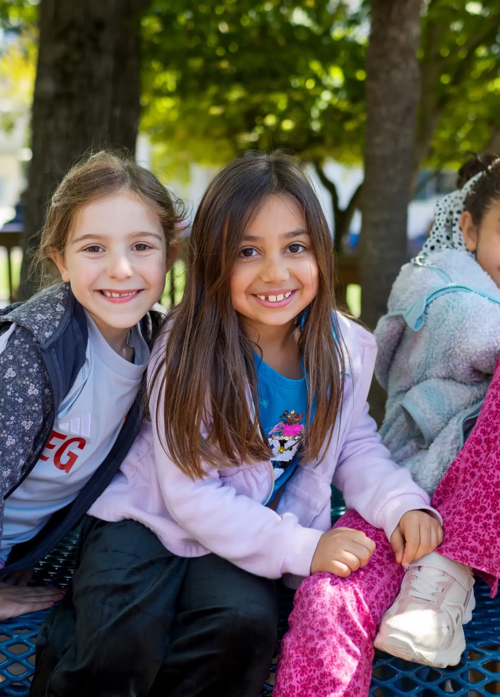 Lower School girls sitting together and smiling at blue picnic tables. 