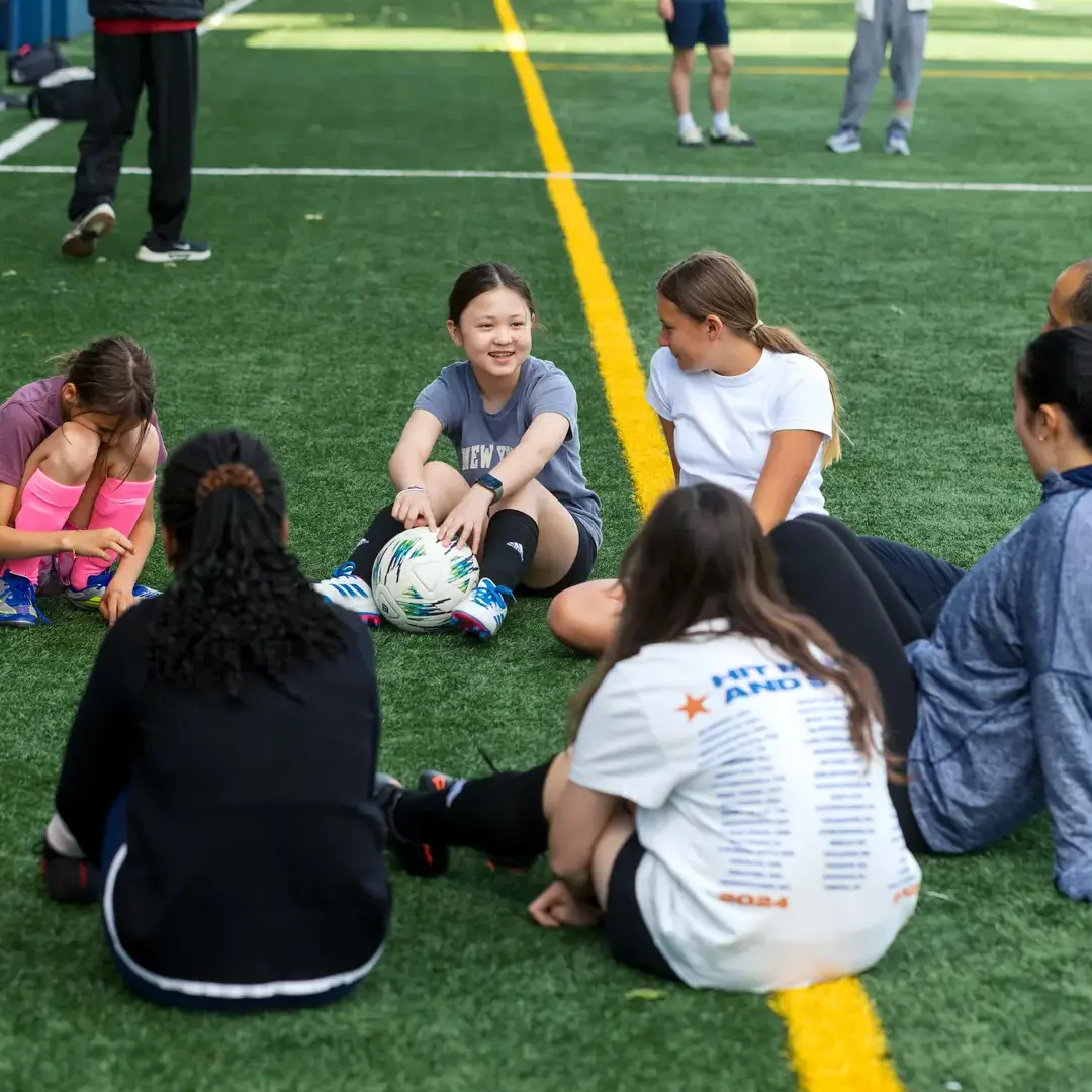 A group of Middle School girls sit on the Athletic Field during a sports practice at the Upper School.