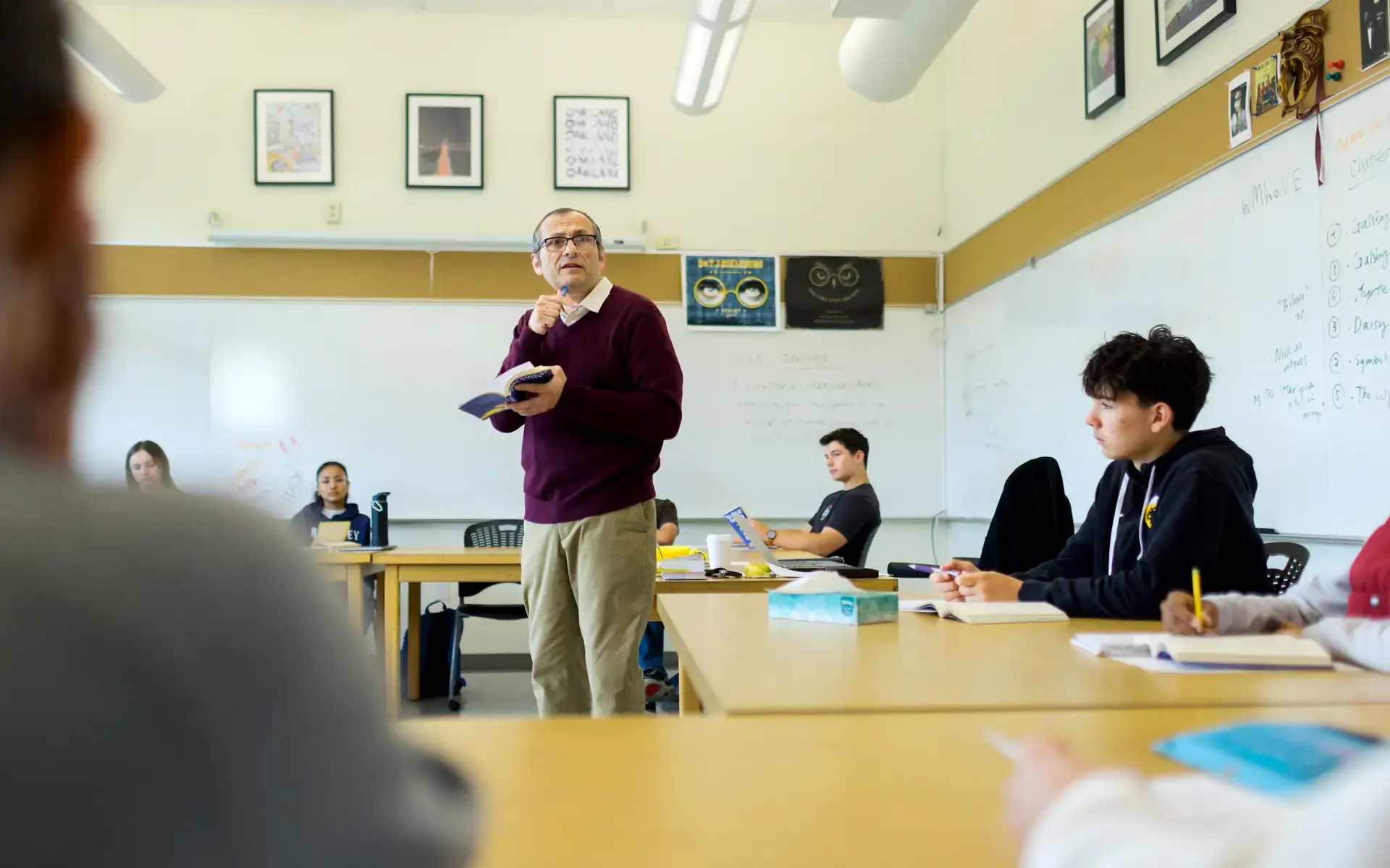 An Upper School teacher stands in the middle of the classroom, leading an English seminar with students sitting at desks surrounding him. 
